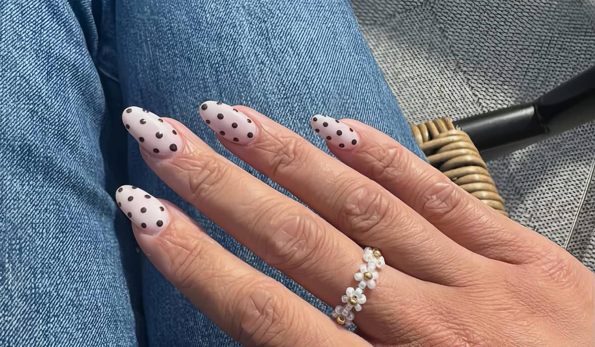 Black polka-dot French tips on long almond nails against denim